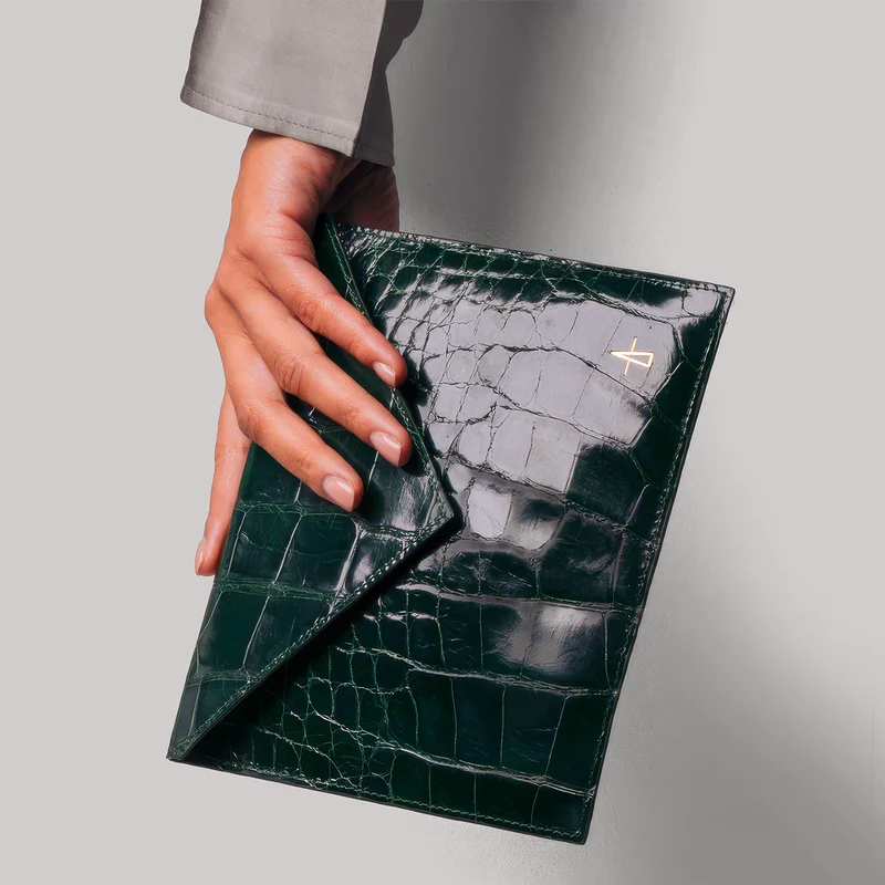 Hands holding a green crocodile-embossed leather clutch