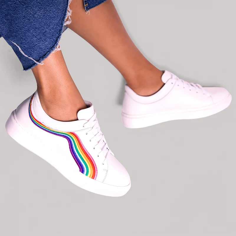 White leather sneaker with a rainbow side stripe, worn
